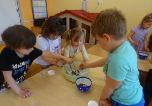 Dzieci mieszają łyżkami sól z płatkami kwiatów w misce.